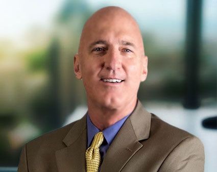 Bald man in a suit and tie smiling with a blurred background.
